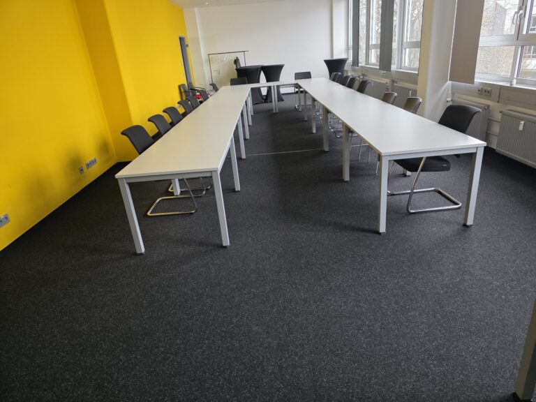Büro mit Schreibtischen, Stühlen und gelber Wand