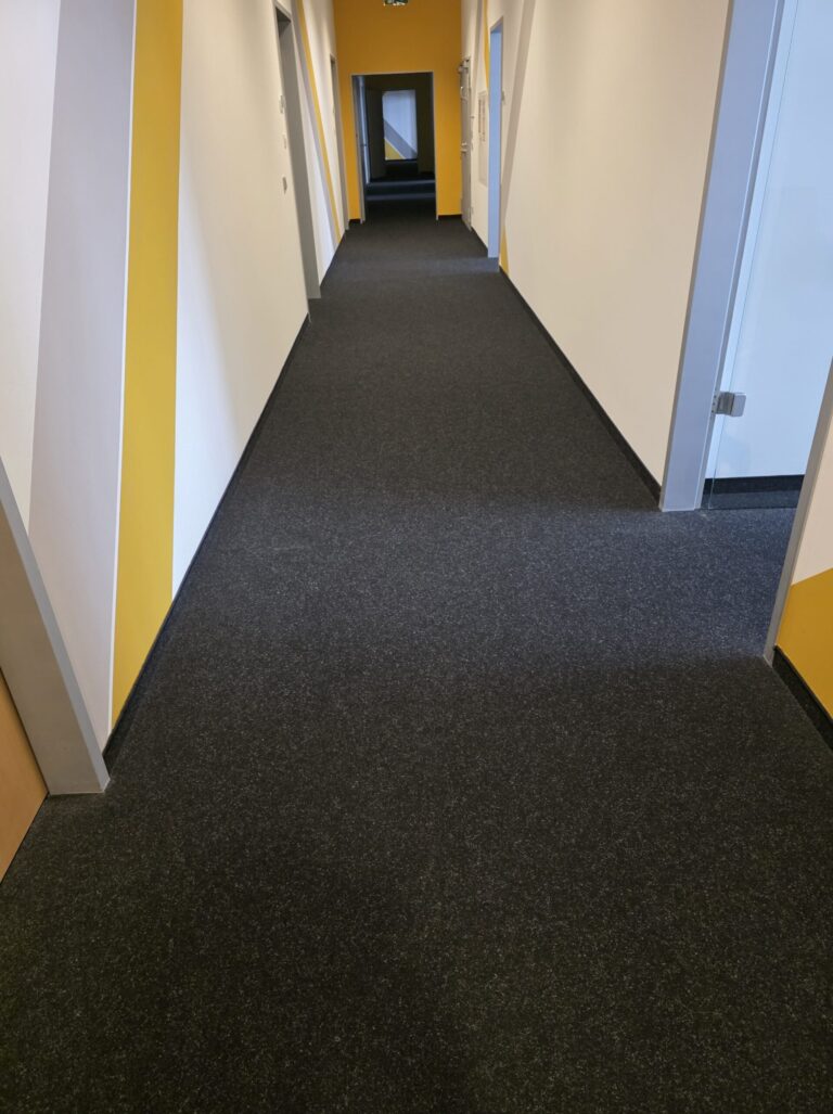 Büroflur mit gelber Wand und dunklem Teppichboden