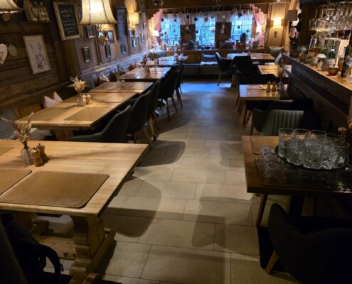 Gaststube mit gedeckten Holztischen und sauberem Fliesenboden