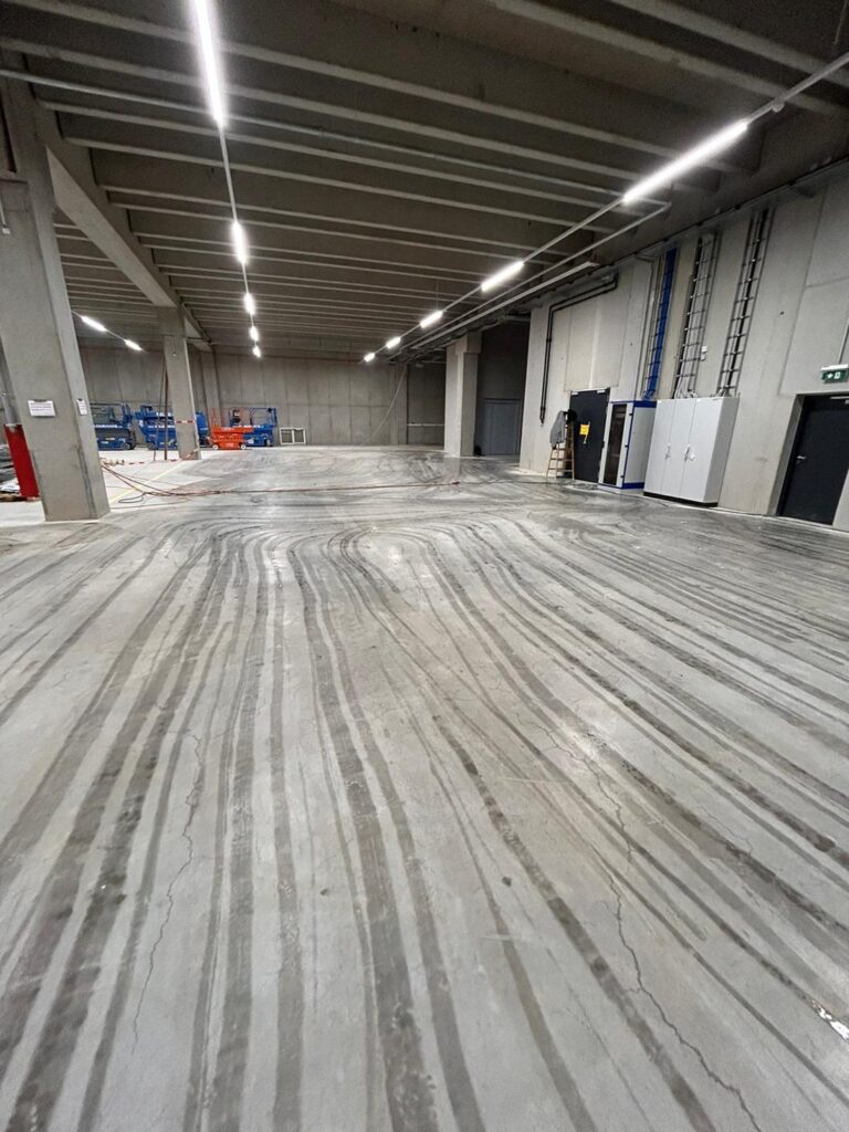 Baustellenreinigung: langer Hallengang mit Reifenspuren vor der Reinigung