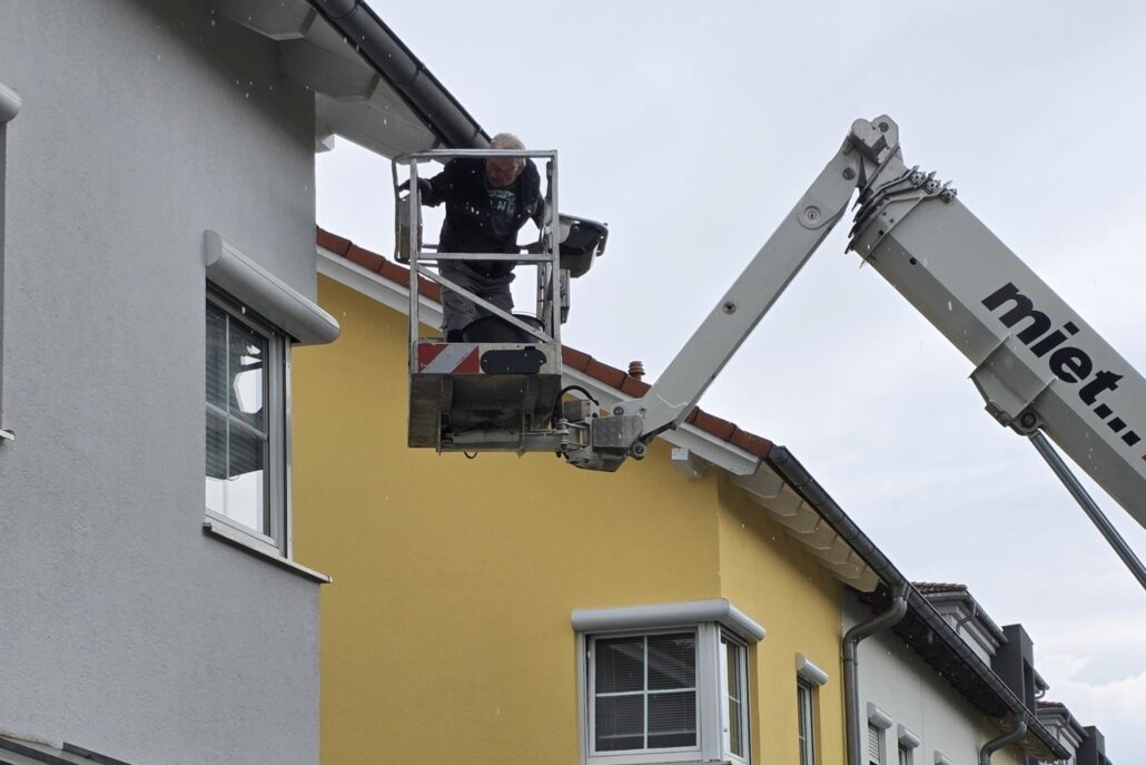 Hubarbeitsbühne an der Dachrinne eines gelben Wohnhauses
