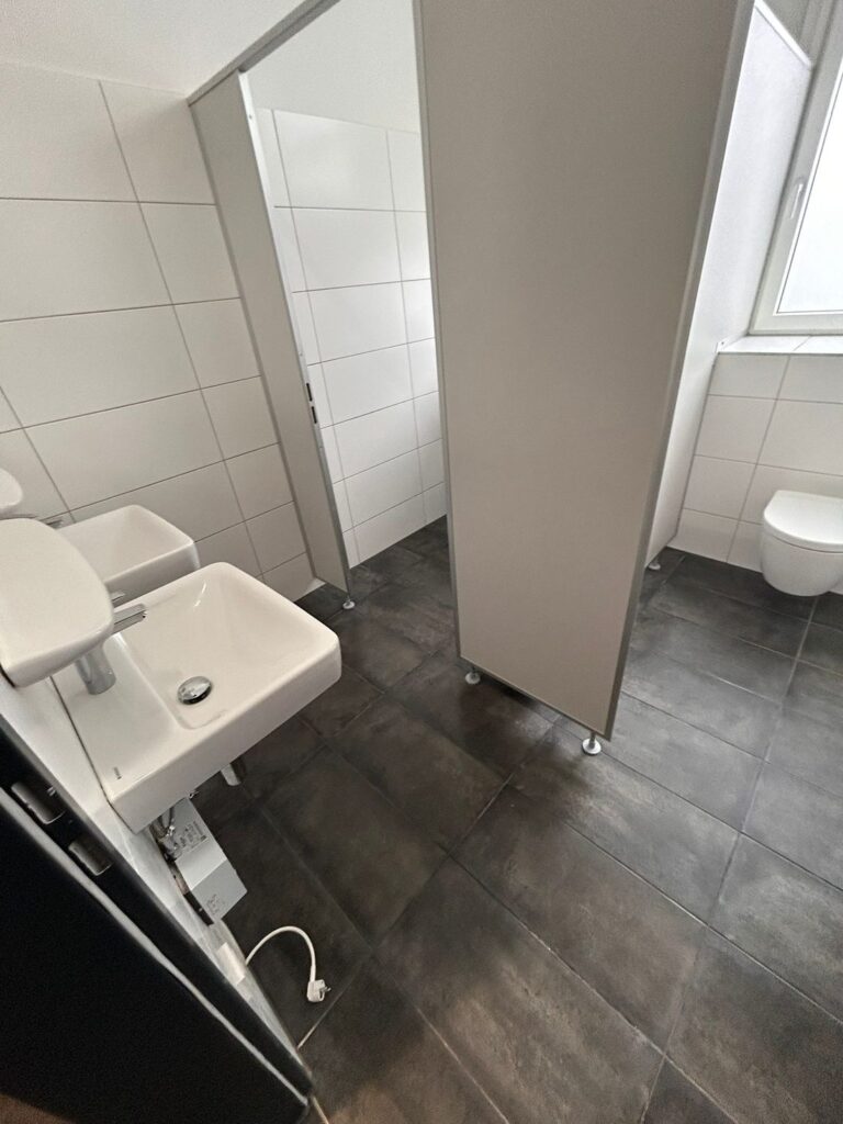 Gereinigte WC-Kabine mit Waschbecken und dunklen Bodenfliesen