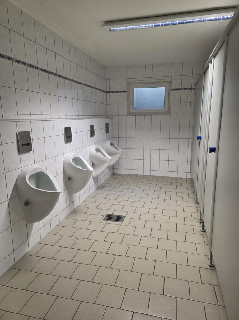 Sanitärreinigung: geflieste WC-Anlage mit Urinalen und Kabinen