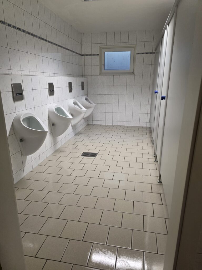Sanitärreinigung: WC-Anlage mit Urinalen und frisch gewischtem Fliesenboden